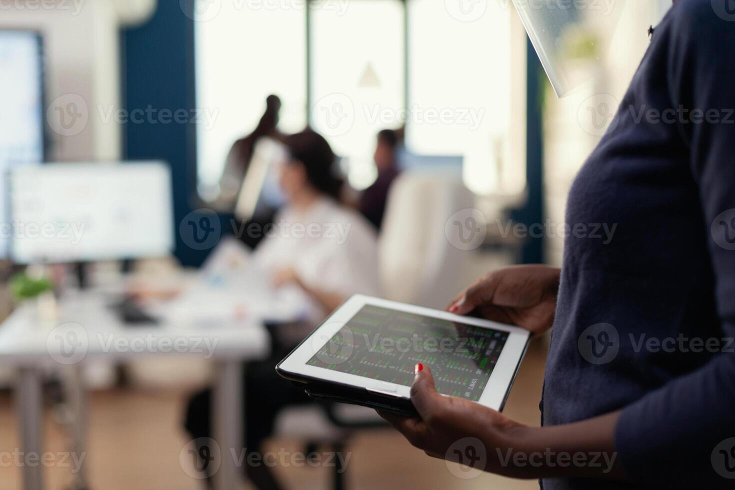 African businesswoman checking corporate graph on tablet pc. Multiethnic coworkers respecting social distance in business company during global pandemic with coronavirus. photo