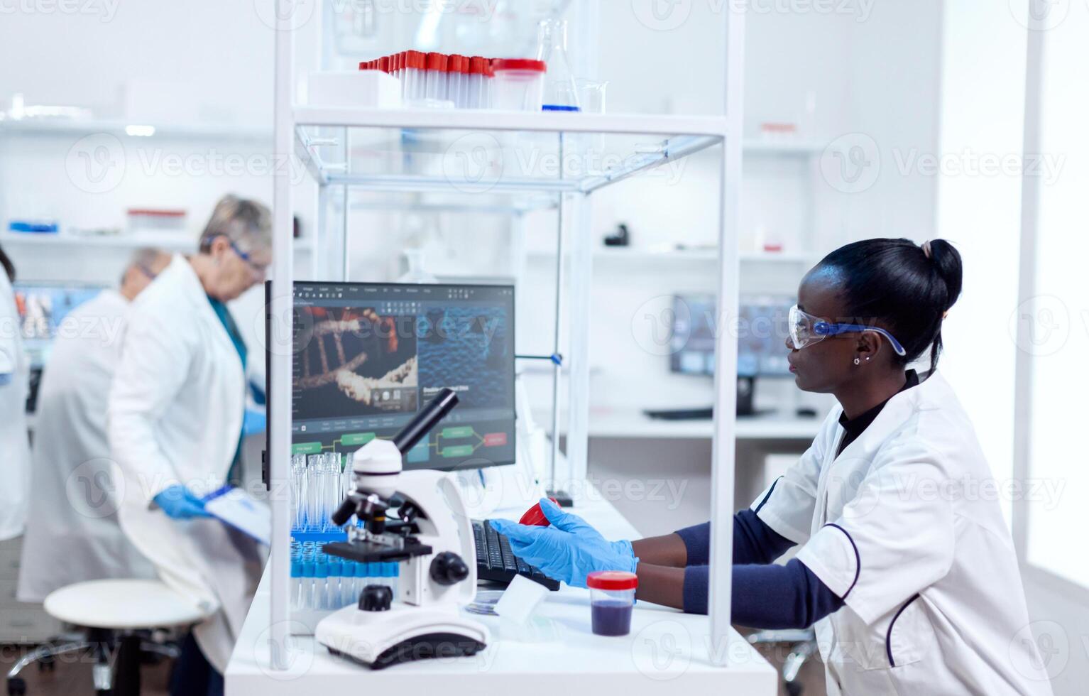 Scientist with african ethnicity conducting virus analysis with her team in modern facility. Black healthcare researcher in biochemistry laboratory wearing sterile equipment. photo