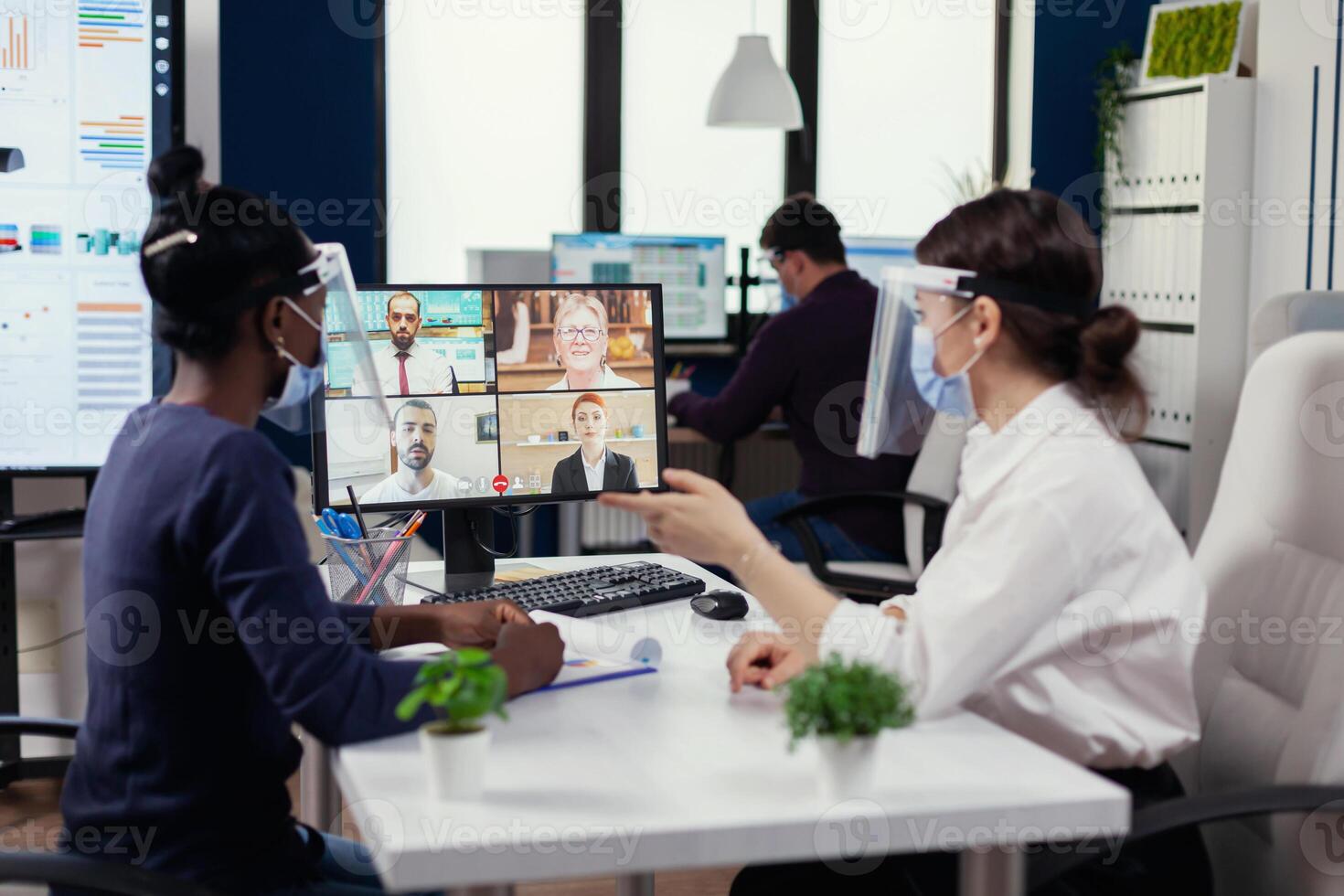 Black woman and coworker having a financial video call with business people. New normal business office. Multiethnic team working respecting social distance during global pandemic with coronavirus. photo