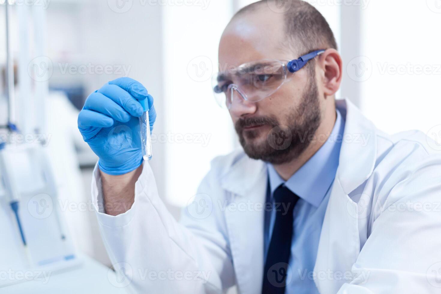 Concentrated scientist in laboraty conducting sample reseach. Researcher in biotechnology sterile lab holding analysis in tube wearing gloves and protection glasses. photo