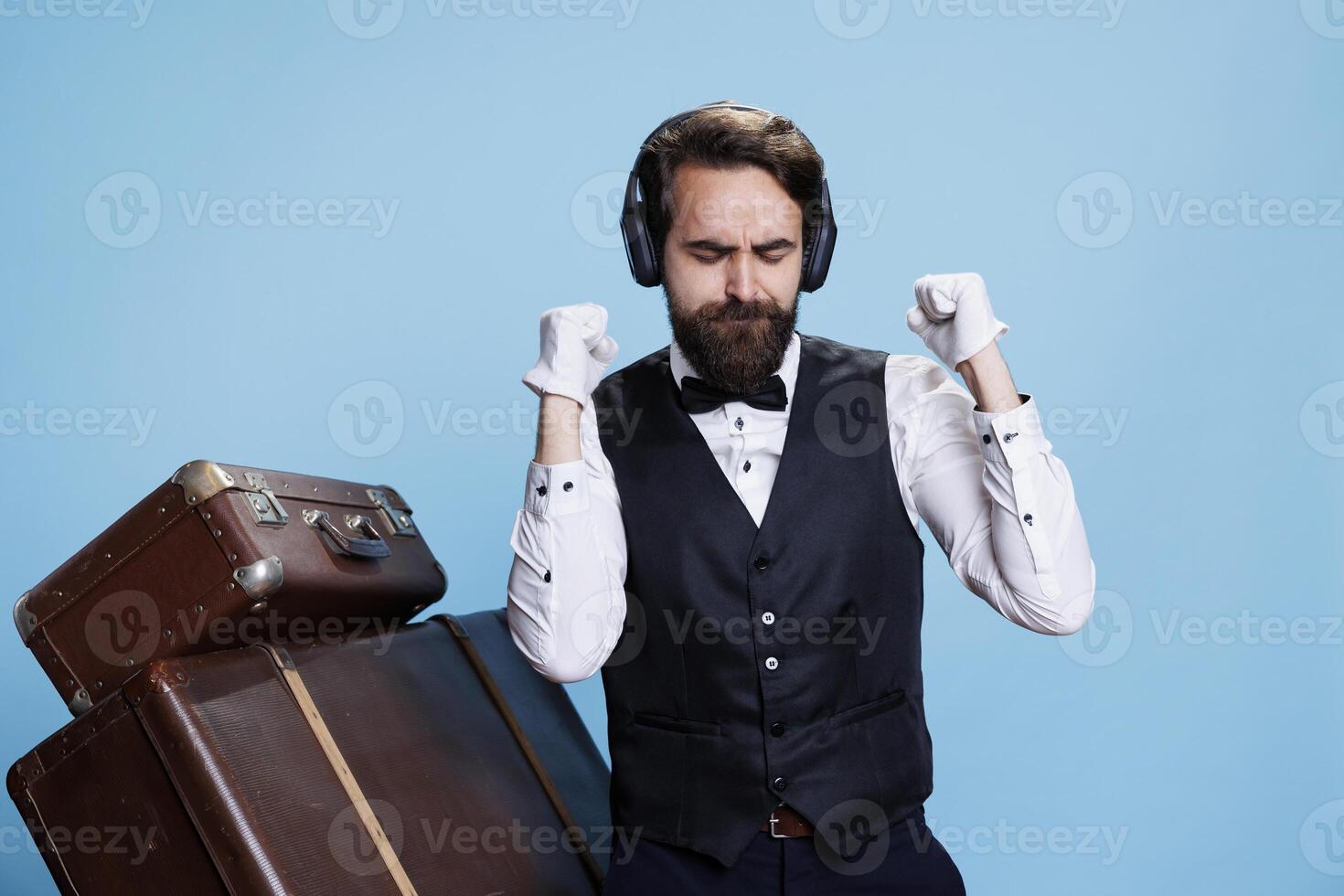 gracioso portero escucha a música en estudio, teniendo divertido bailando con traje y atar. profesional elegante hotel empleado lo hace danza se mueve en canciones mediante audio auriculares, viaje sector. foto