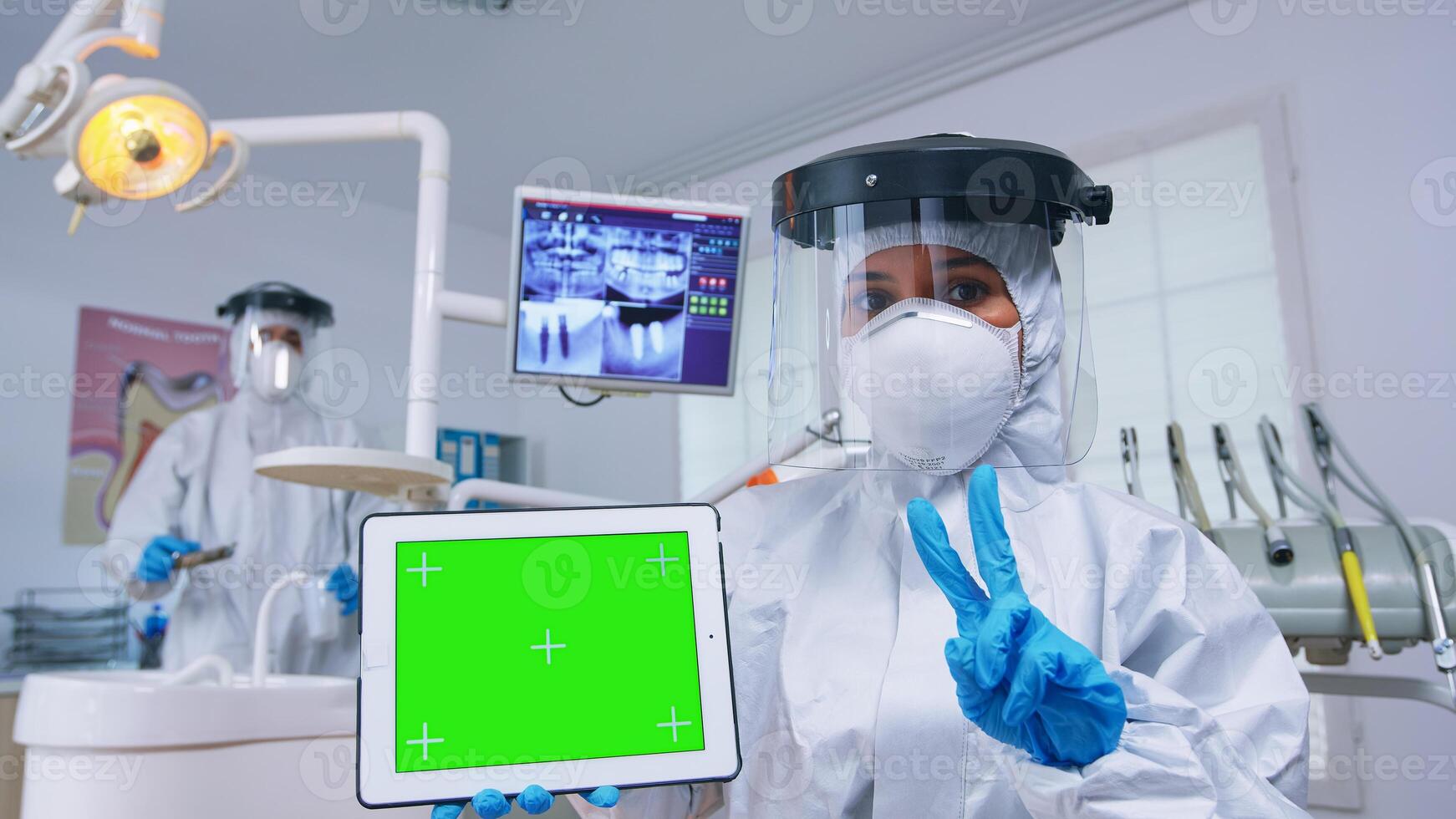 Patient pov of dentist in ppe suit explaining dental radiography and diagnosis for teeth infection using tablet with green screen. Stomatology specialist pointing at mockup, copy space, chroma display photo