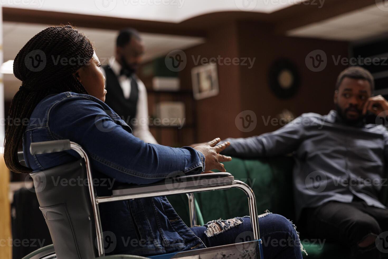 Disabled hotel guest sitting in lobby, African American woman in wheelchair at sitting area in foyer, acomodations for travelers with reduced mobility. Disability access in hospitality industry photo