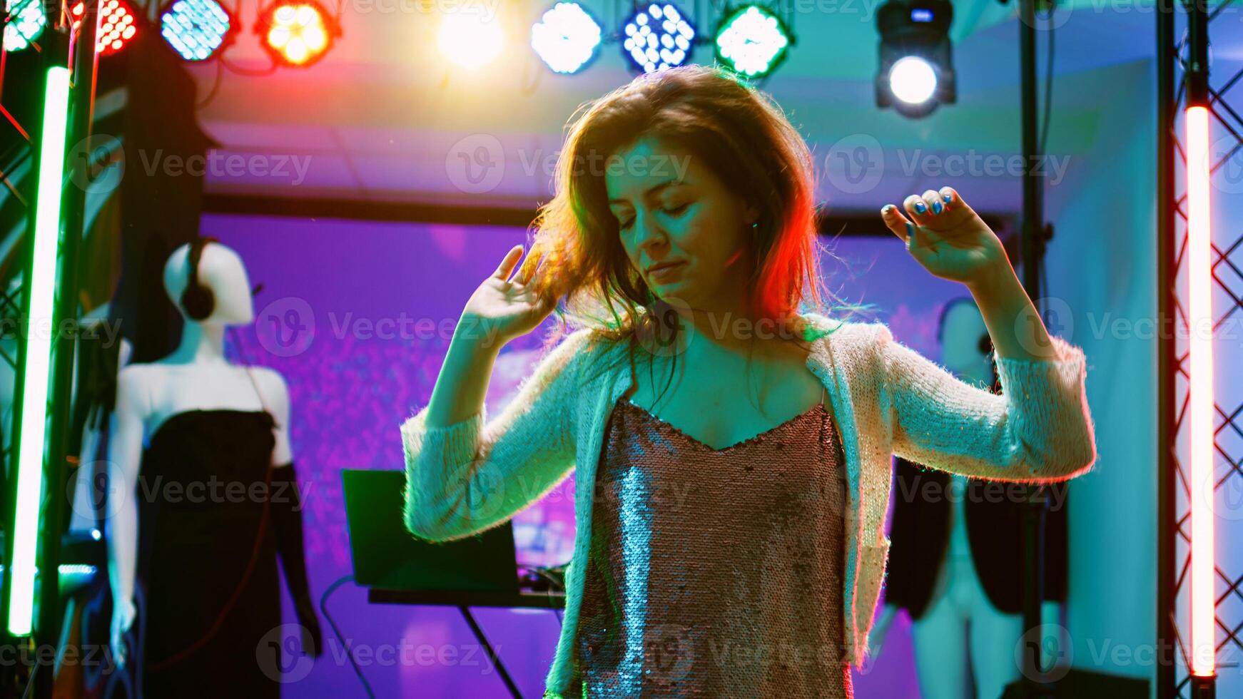 Young person dancing at nightclub, showing cool dance moves in discotheque with funky music. Cheerful girl partying and having fun at electronic party, stage lights on dance floor. Handheld shot. photo