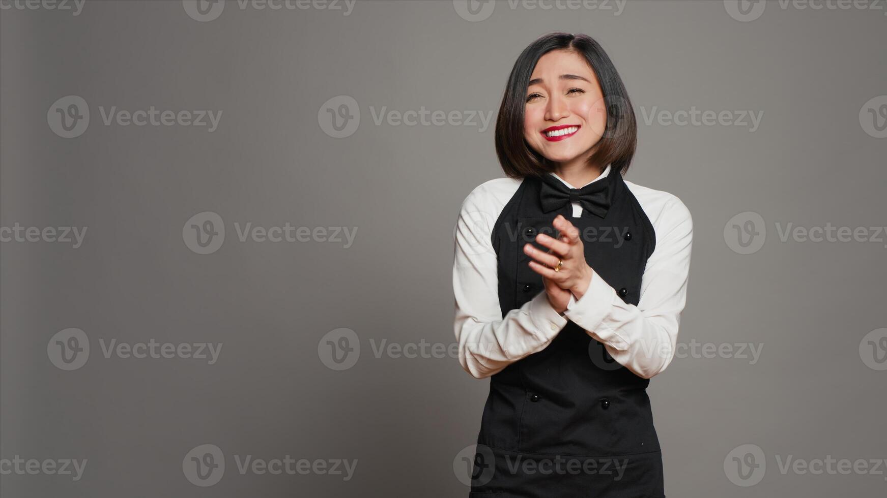 Asian server applauding someone and cheering for success, saying congratulations in front of camera. Waitress in formal uniform clapping hands, doing standing ovation gesture. Camera A. photo