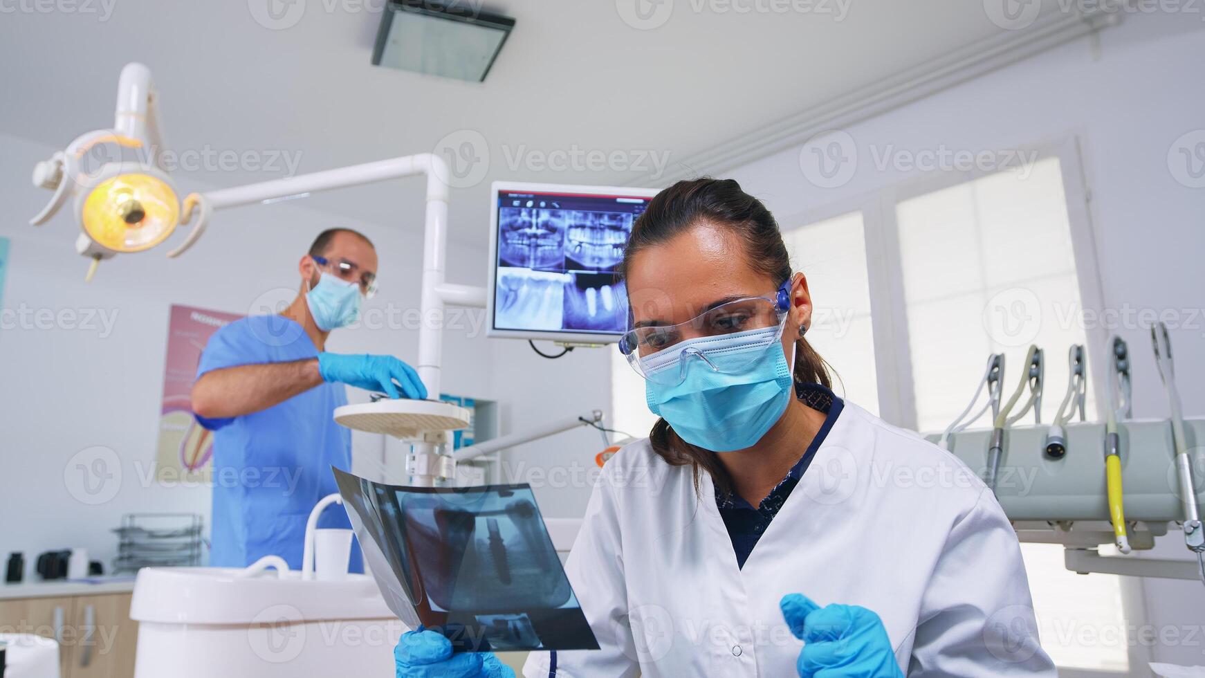 paciente pov en dental oficina explicando tratamiento de dientes cavidad, dentista señalando en radiografía imagen. estomatología médico vistiendo protector máscara y guantes, trabajando en moderno estomatológico clínica foto