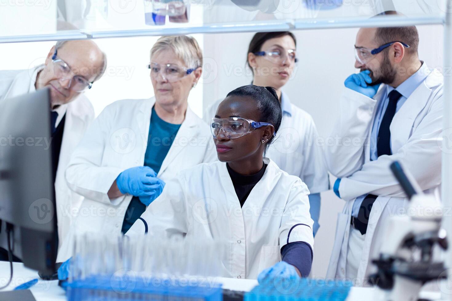 Chemists biologists conducting medical analysis using computer. African healthcare researcher in biochemistry laboratory wearing sterile equipment. photo