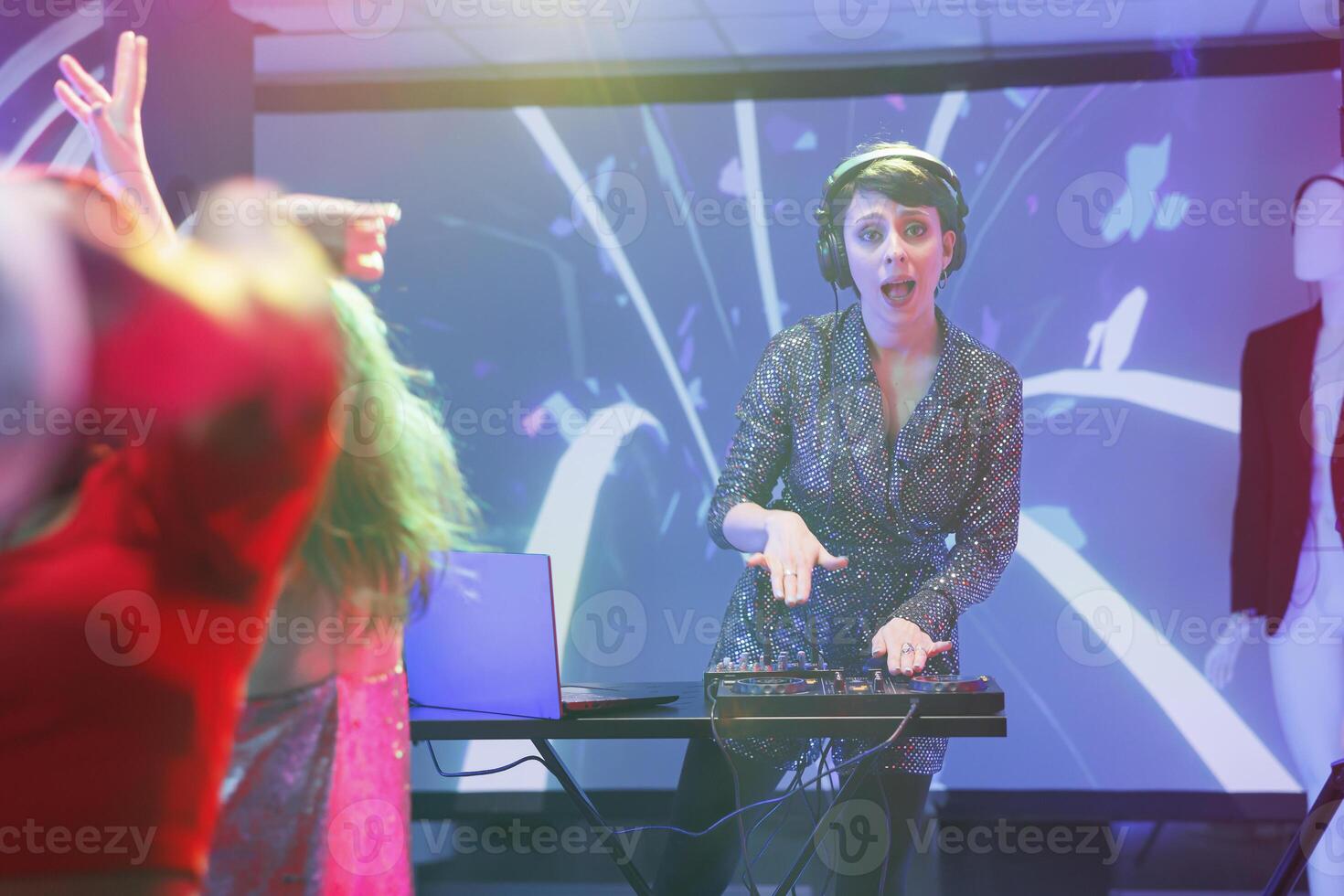 Excited woman dj mixing music using jog wheels on controller while performing on nightclub stage portrait. Young musician playing at discotheque party in club and looking at camera photo