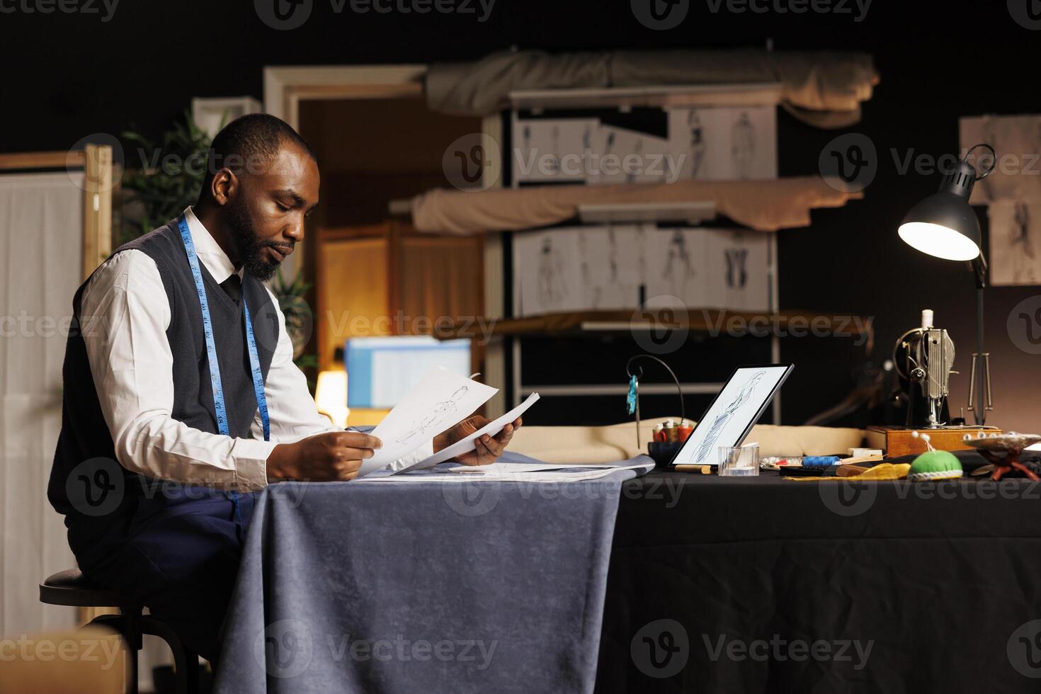 Couturer looking over sketch drawings, trying to pick best design for upcoming haute couture fashion collection. Fashion designer working on bespoken garments in atelier studio photo