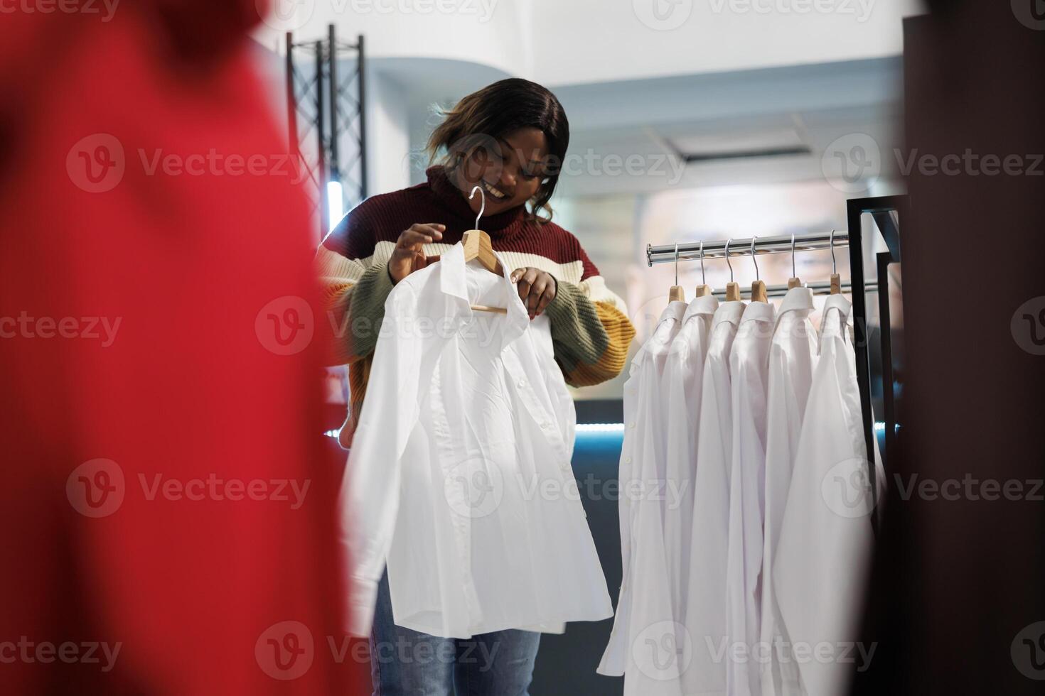 ropa Tienda comprador molesto en camisa mientras explorador formal vestir para armario. africano americano mujer participación atuendo en percha, examinando tamaño, estilo y ajuste mientras compras en boutique foto