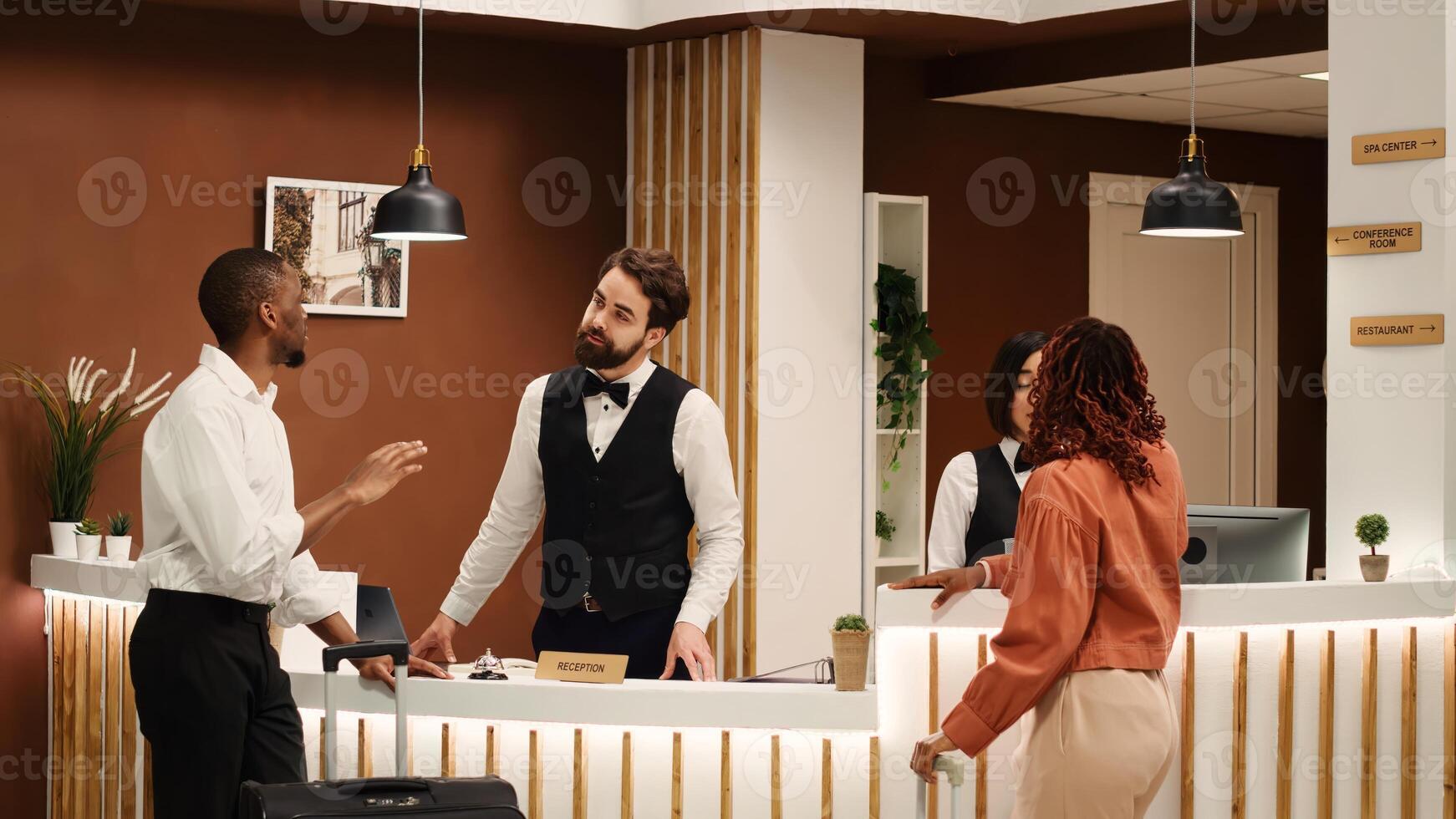 Helpful front desk receptionists answering customer inquiries about hotel facilities during guests check in process. Cheerful smiling concierge coworkers assisting visitors with room registration photo