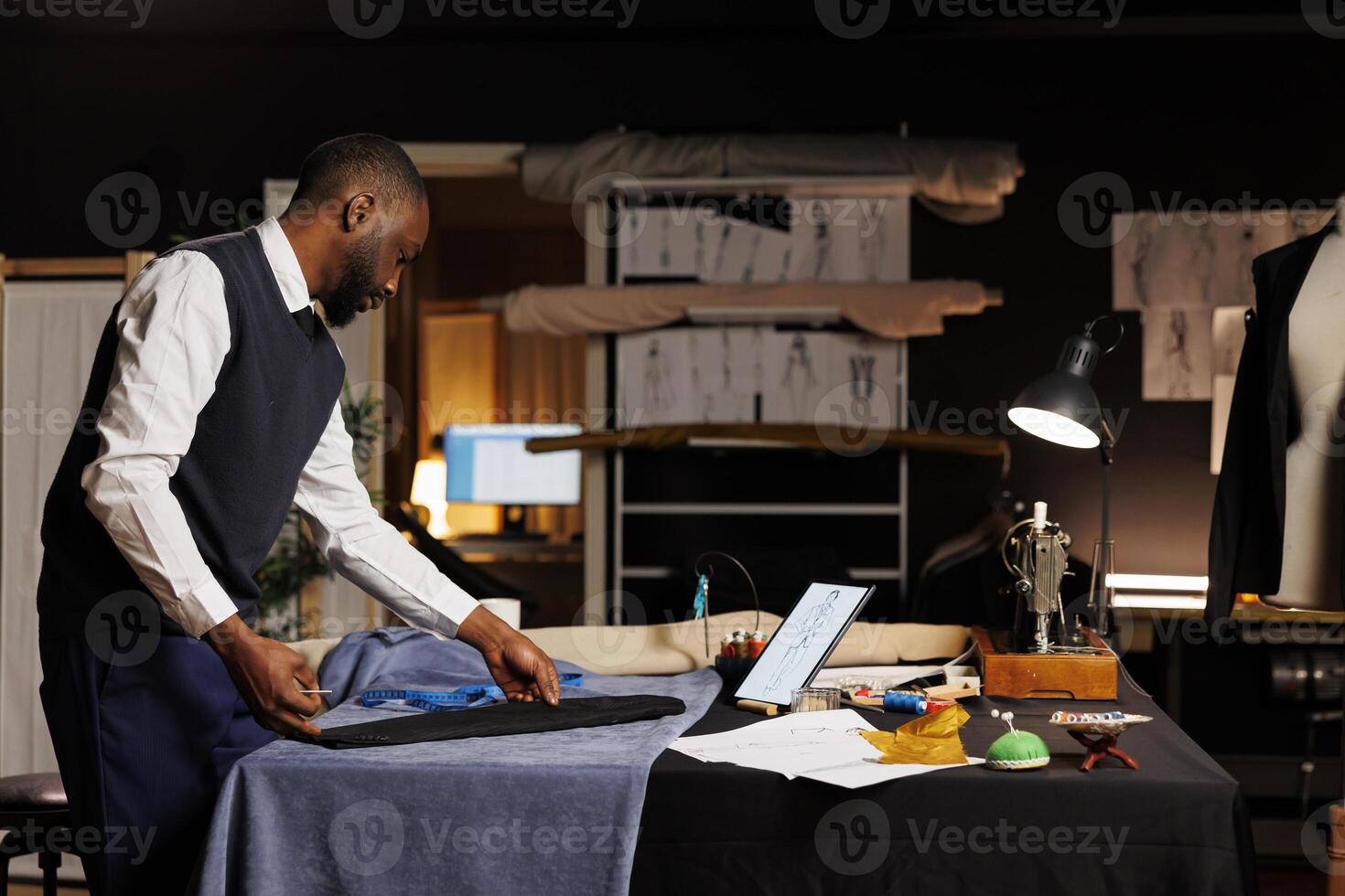 Expert suitmaker stiching together bespoken business suit, looking online for inspiration. Skilled couturier working in professional atelier shop, creating premium quality custom made clothing piece photo