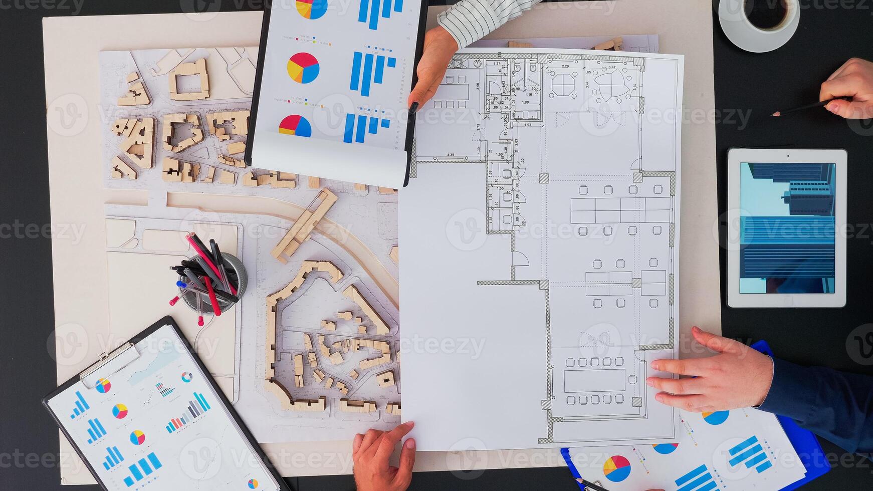 Top view of businesspeople team of architects with buildings prototype, gadgets and papers working at office table. Engineers brainstorming using modern device on copy space, flat lay concept photo