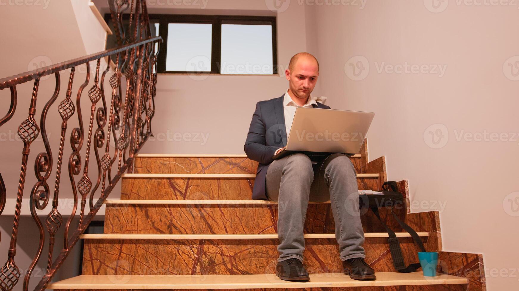 sobrecargado de trabajo oficina ejecutivo sentado en escalera mecanografía en ordenador portátil mirando en documentos desde portapapeles mientras colegas Moviente en escalera. profesional gente de negocios trabajando en moderno financiero edificio foto