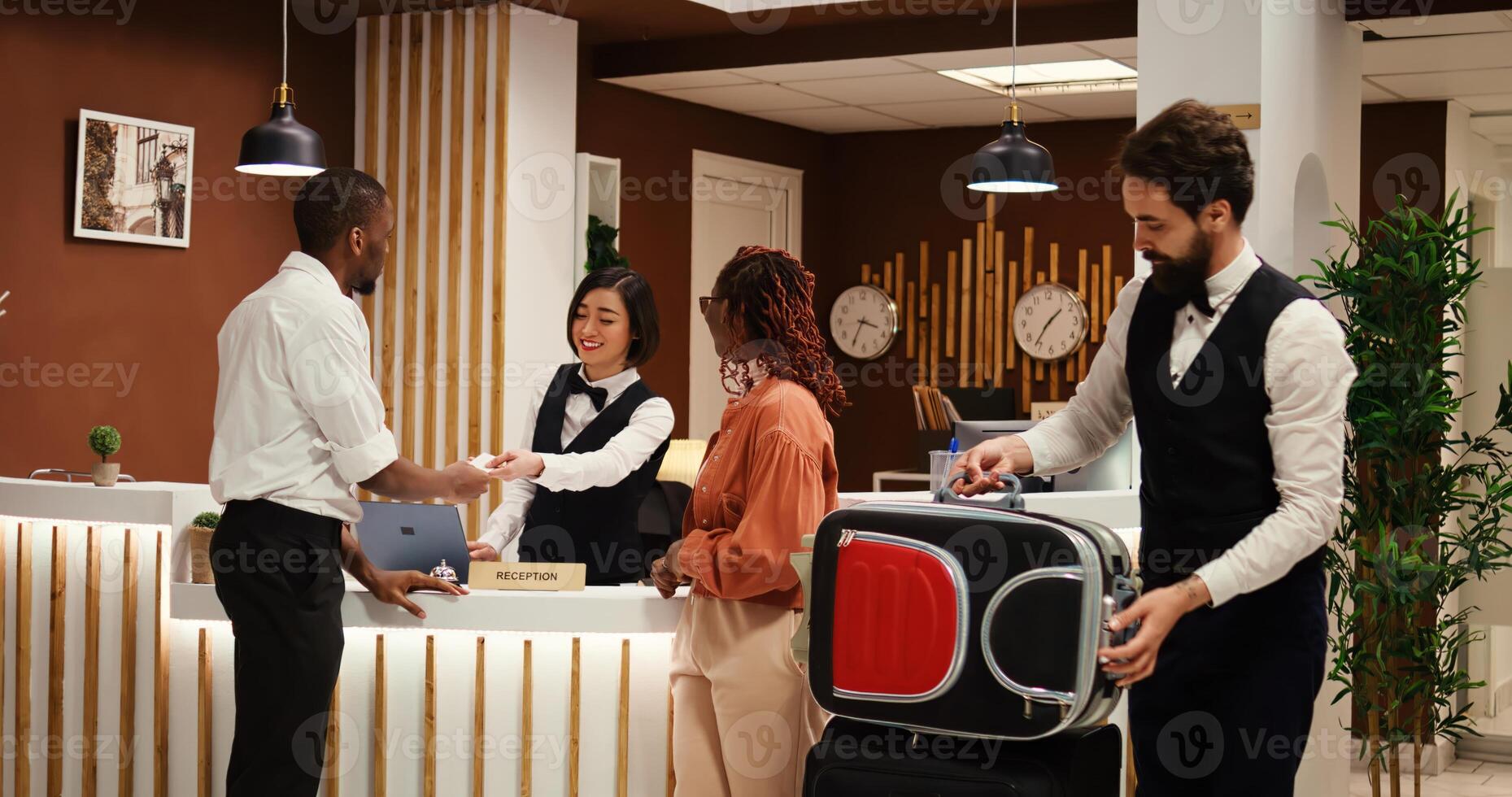 Guests checking out from resort, handing over room access card key while friendly bellboy helps them with their baggage. Happy relaxed tourists leaving hotel after nice stay photo