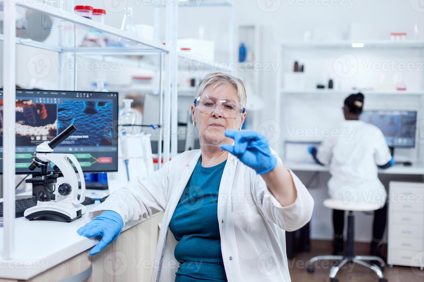 Senior scientist in modern laboratory holding genetic sample on laboratory glass. Elderly researcher in sterile lab looking on microscope slide wearing lab coat. photo