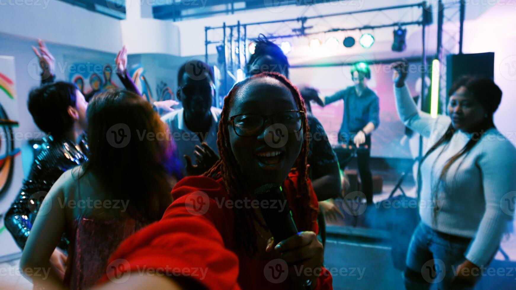 POV of woman filming vlog at discotheque, recording video while she dances with joyful group of friends. Cheerful girl having fun with people at disco party, entertainment. Handheld shot. photo