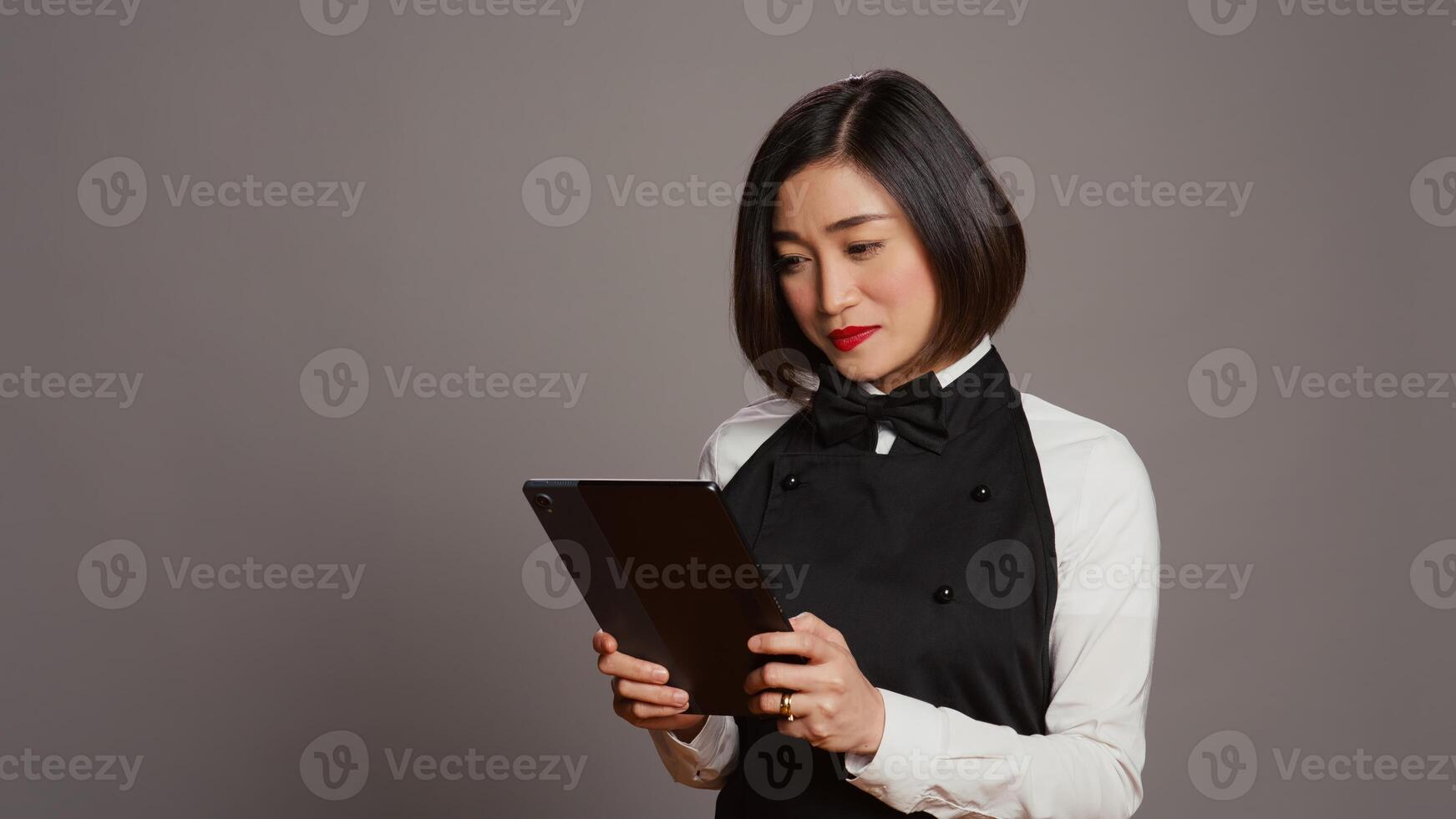 Asian restaurant server checking all table reservations on tablet, browsing through clients information on website. Waitress looking at online webpages to see availability. Camera B. photo