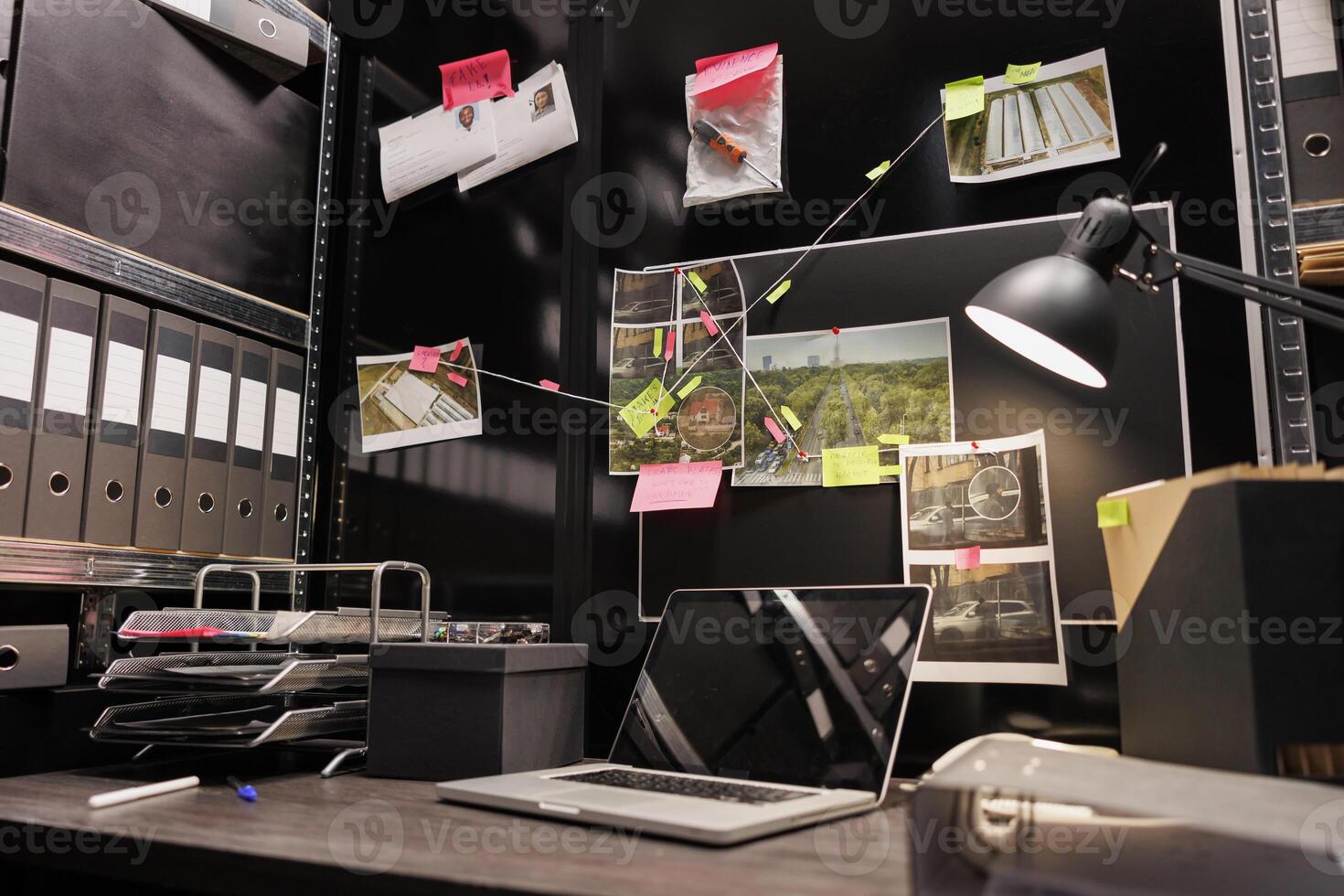 Empty dark police detective room with murder case investigation process on board. Suspect photographs connected with clues hanging on wall and file folders on racks in investigator agency office photo