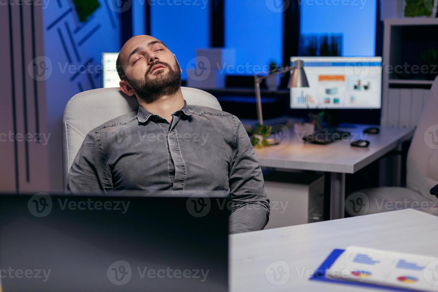 Exhausted hardworking businessman sleeping on chair. Workaholic employee falling asleep because of working late at night alone in the office for important company project. photo