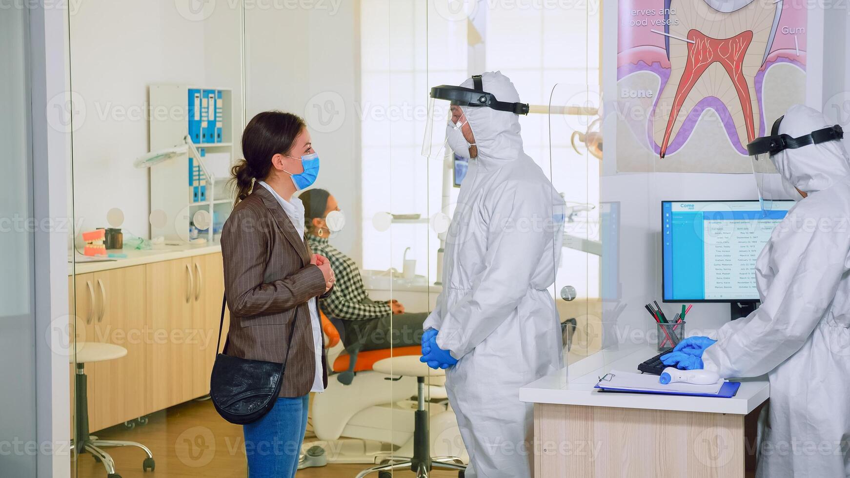 Dentist doctor with overall explaining teeth treatment to patient in waiting area, planning surgery steps during global pandemic. Concept of new normal dentist visit in coronavirus outbreak. photo