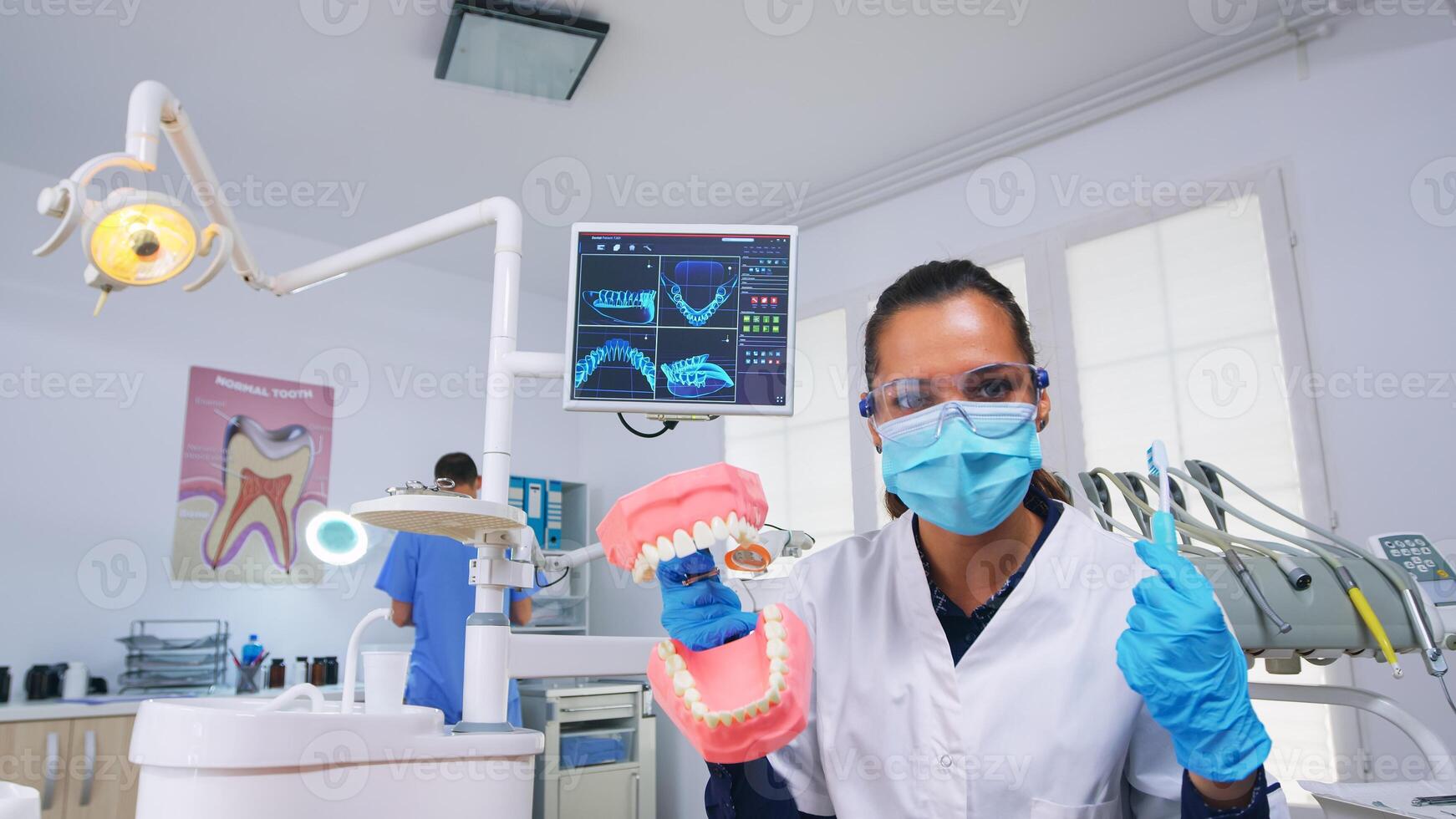 Patient pov of dentist teaching woman correct cleaning of teeth in dental office using skeleton accessory. Stomatolog wearing protection mask asking for presentation teeth medical object photo