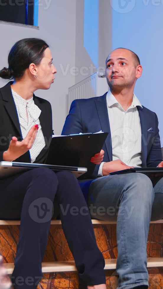 Overworked furious businesswoman on coworker during difficult corporate deadline sitting on stairs. Colleague entrepreneur arguing late in evening at corporate job, explaining finance project. photo