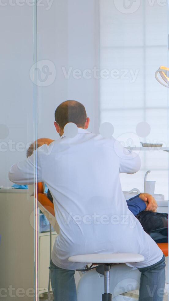 Patients asking for help filling in dental registration form preparing for exemination. Senior woman sitting on chair in waiting area of crowded orthodontist office while doctor working in background photo