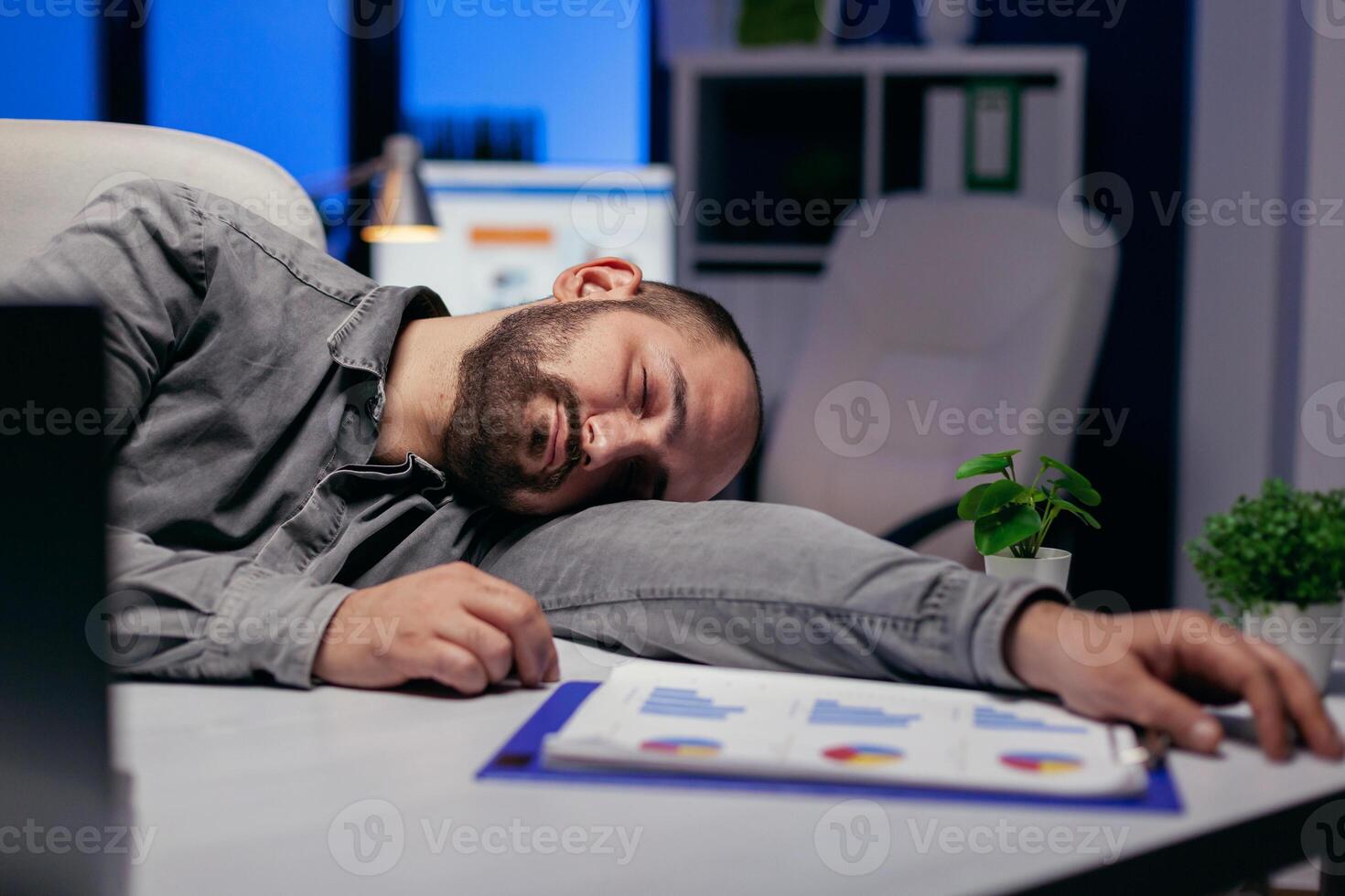 Hardworking entrepreneur sleeps on table at workplace because of deadline. Workaholic employee falling asleep because of while working late at night alone in the office for important company project. photo