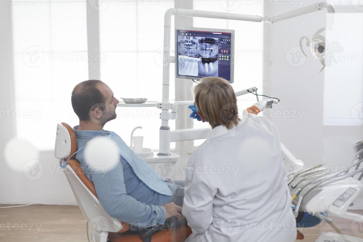 Senior orthodontist woman with face mask explaining dentistry radiography to patient discussing oral treatment to prevent infection during medical examination in dental office. Stomatology concept photo