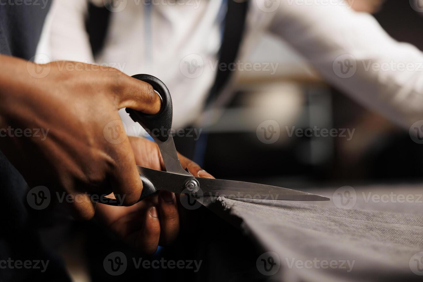 Extreme close up of couturier using scissors to cut refined fabric material in tailoring shop workspace. Experienced suitmaker teaching apprentice expert meticulous craftmanship photo