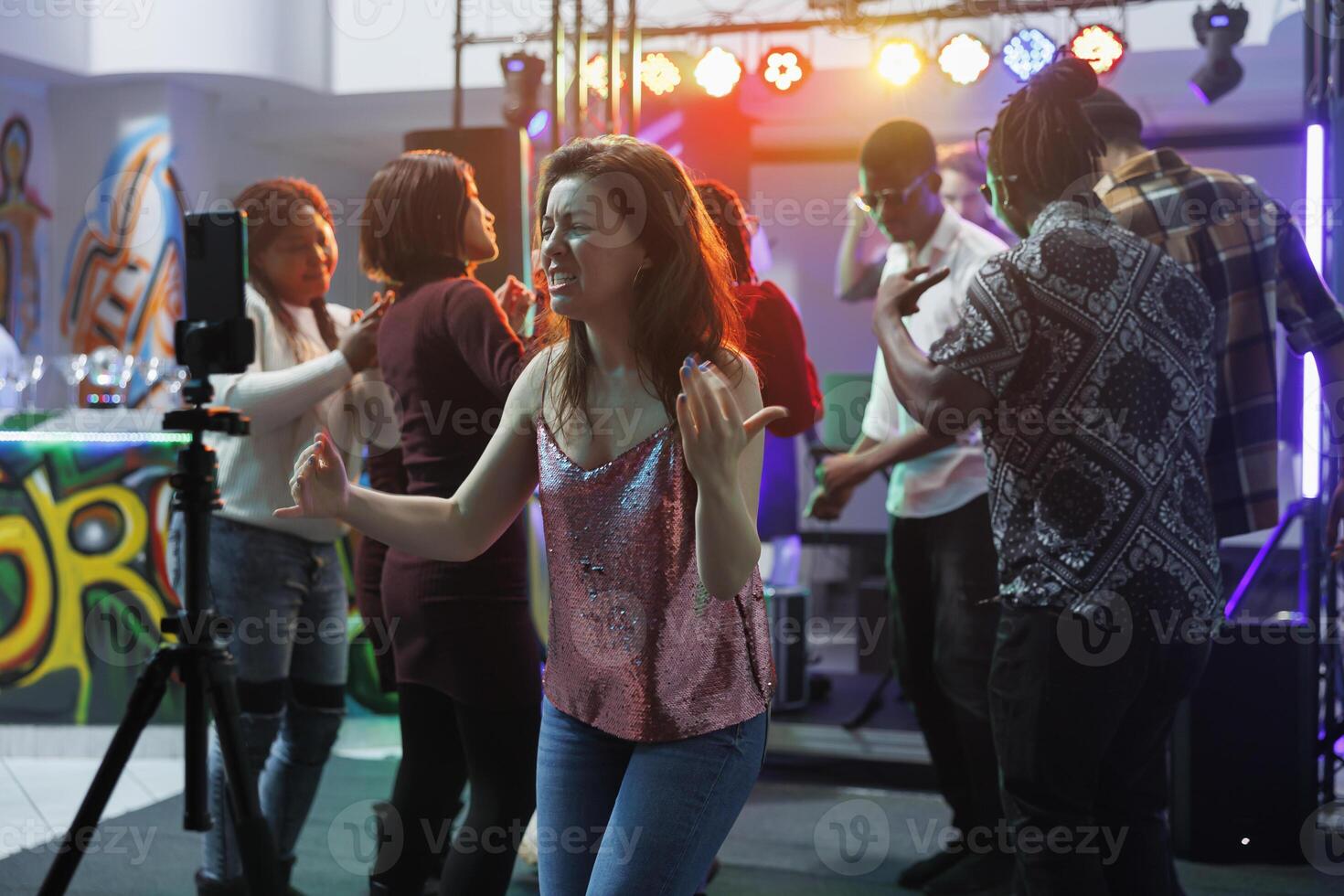 mujer bailando y canto en Club nocturno mientras transmisión en línea en social medios de comunicación utilizando teléfono inteligente en trípode. niña ir de fiesta a club discoteca mientras grabación vídeo en móvil teléfono foto