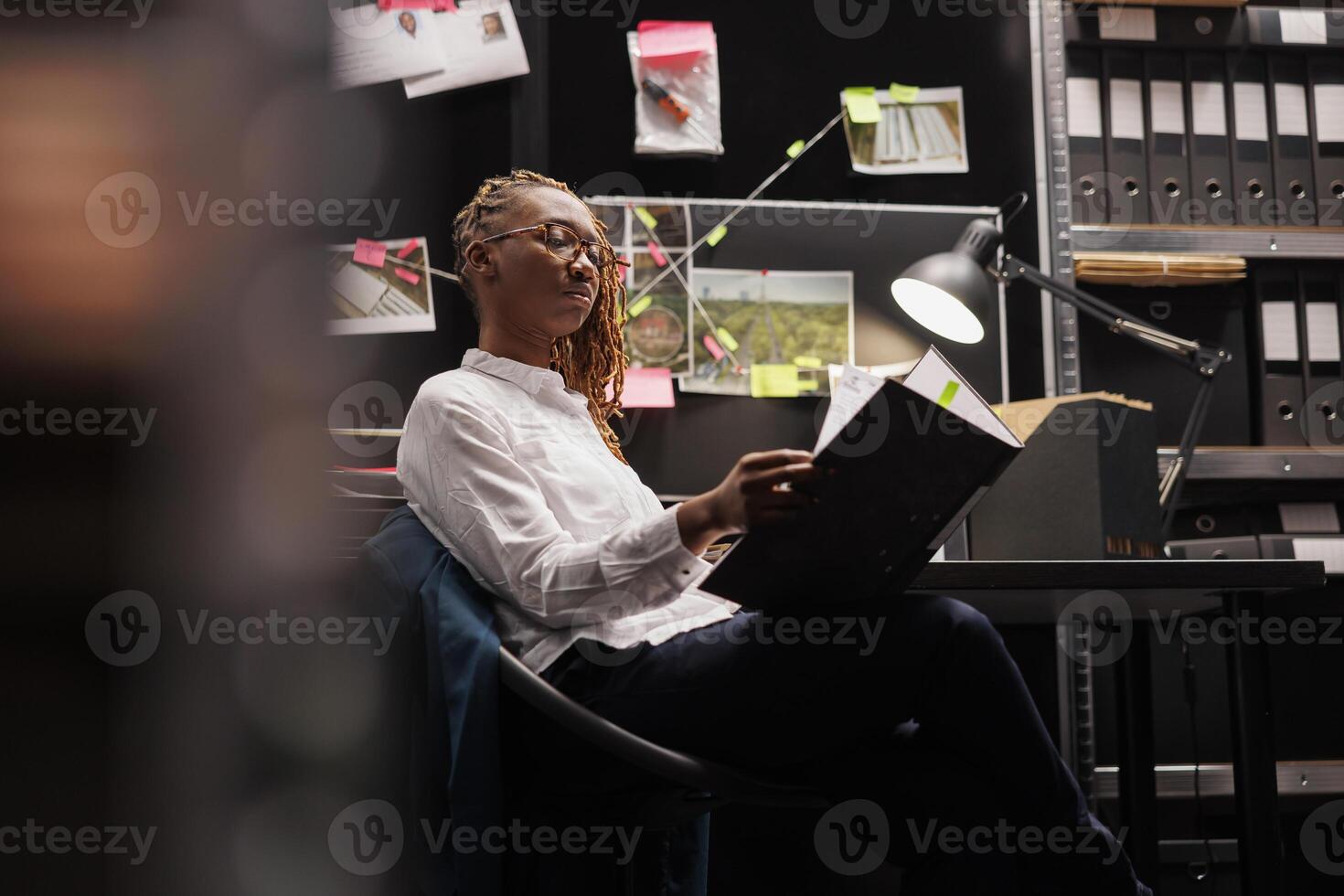 Law enforcement professional studying csi conclusion report in detective office. African american woman police investigator sitting at workplace desk and reading crime case file photo