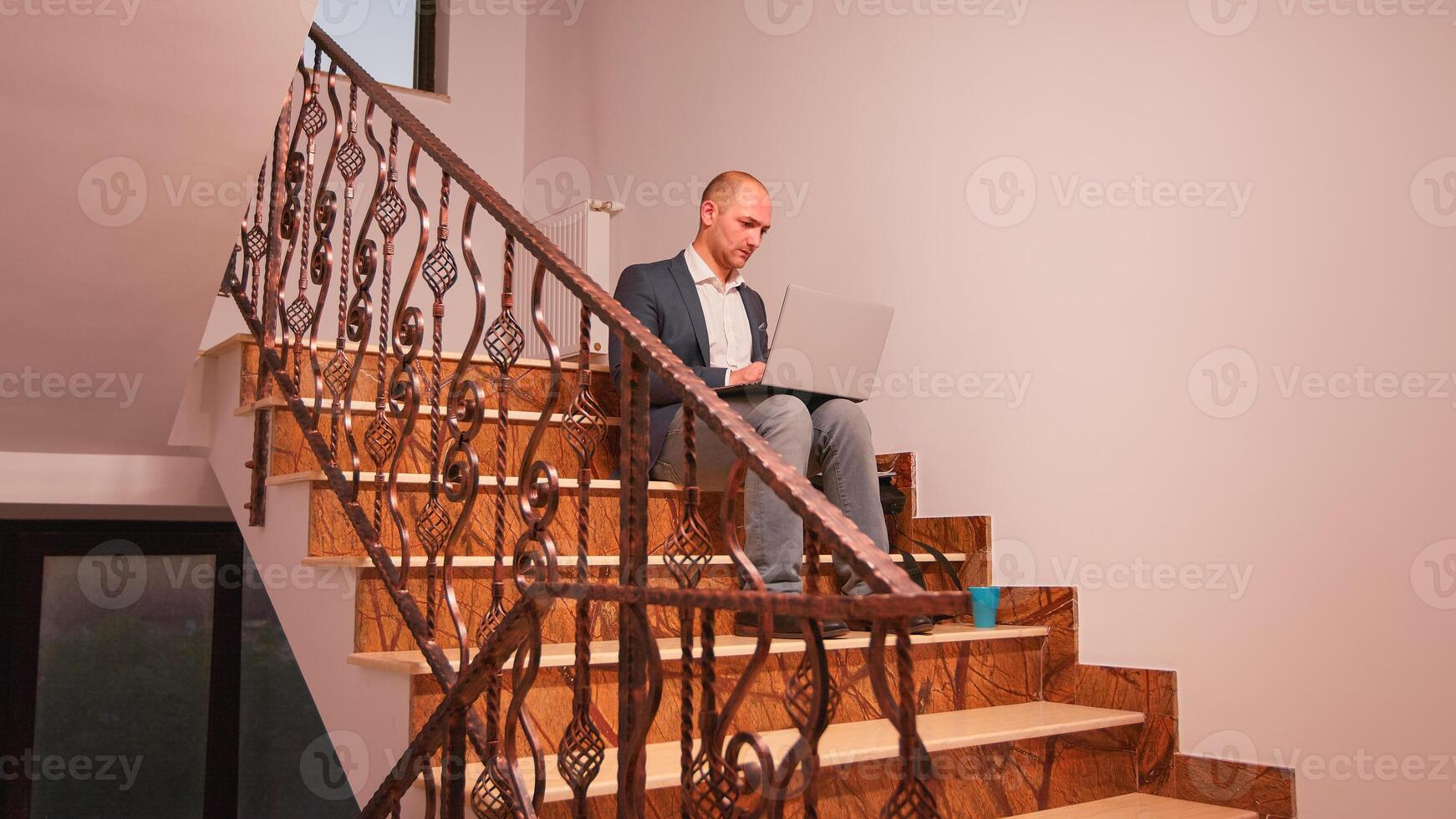 Company manager using laptop overworking on deadline sitting on stairs in finance building. Executive manager doing overtime at job on staircase businesspeople working in modern financial workplac e. photo