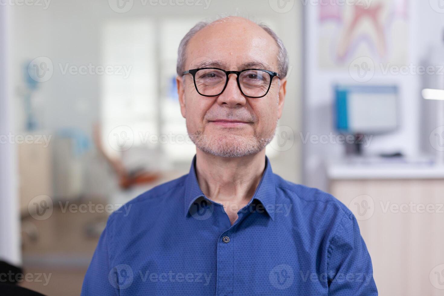 Senior man looking at camera in dental office wainting consultation. Elderly male smiling on webcam sitting on chair in waiting room of stomatological clinic, photo