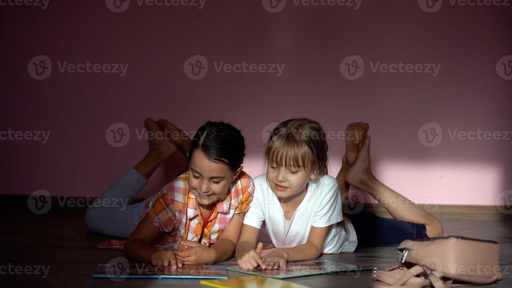 family, leisure and childhood concept - happy sisters lying on floor and doing homework at home photo