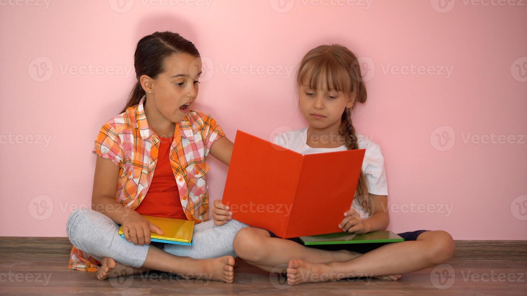 Lovely little girls are reading a book. The concept of education. Isolated on pink background photo