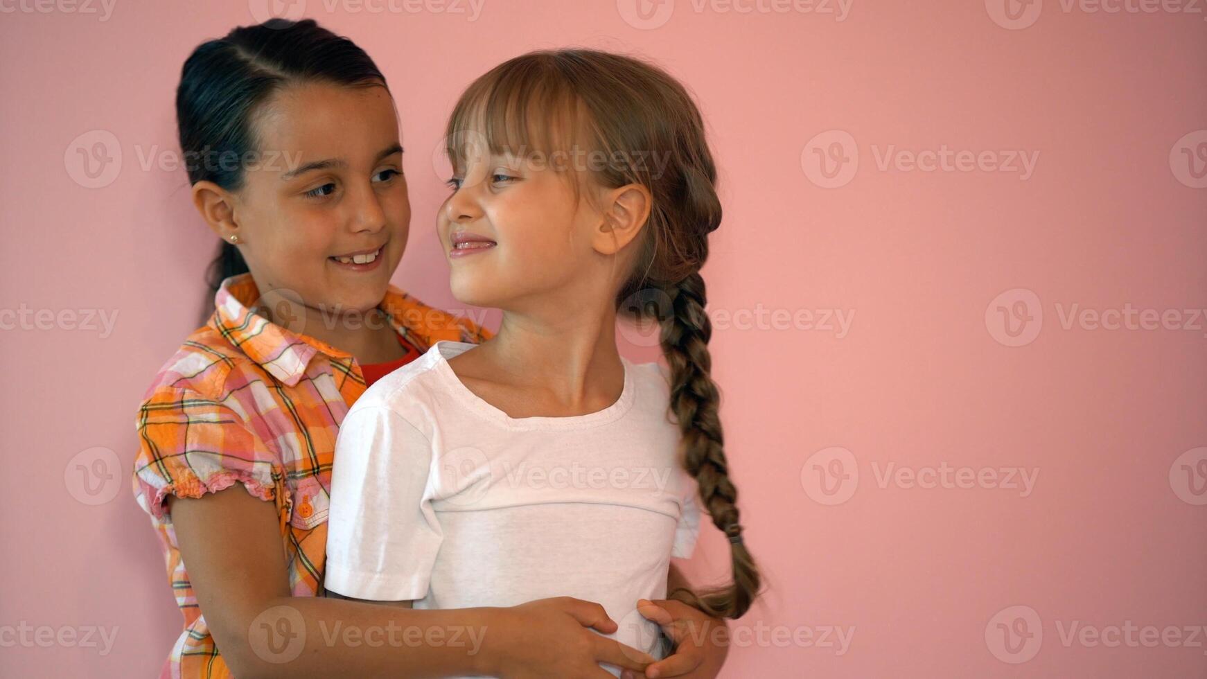 Two happy girls hugging each other isolated on pink background photo