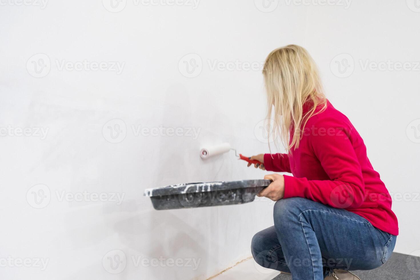 Female decorator painting wall with roller indoors photo