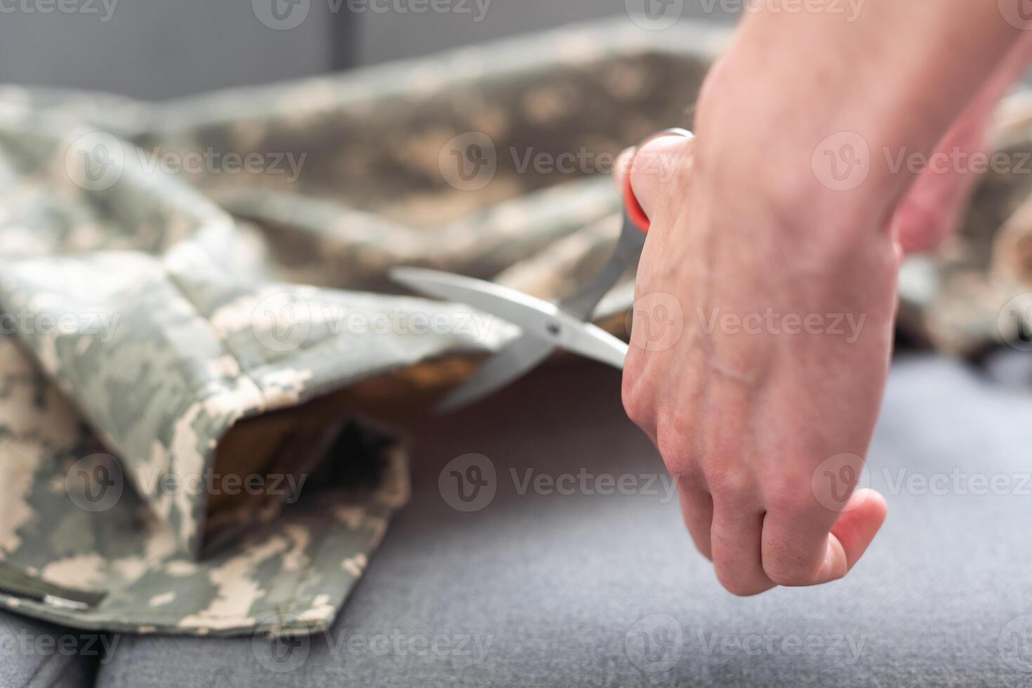Professional tailor cutting camouflage fabric with scissors in workshop, closeup photo