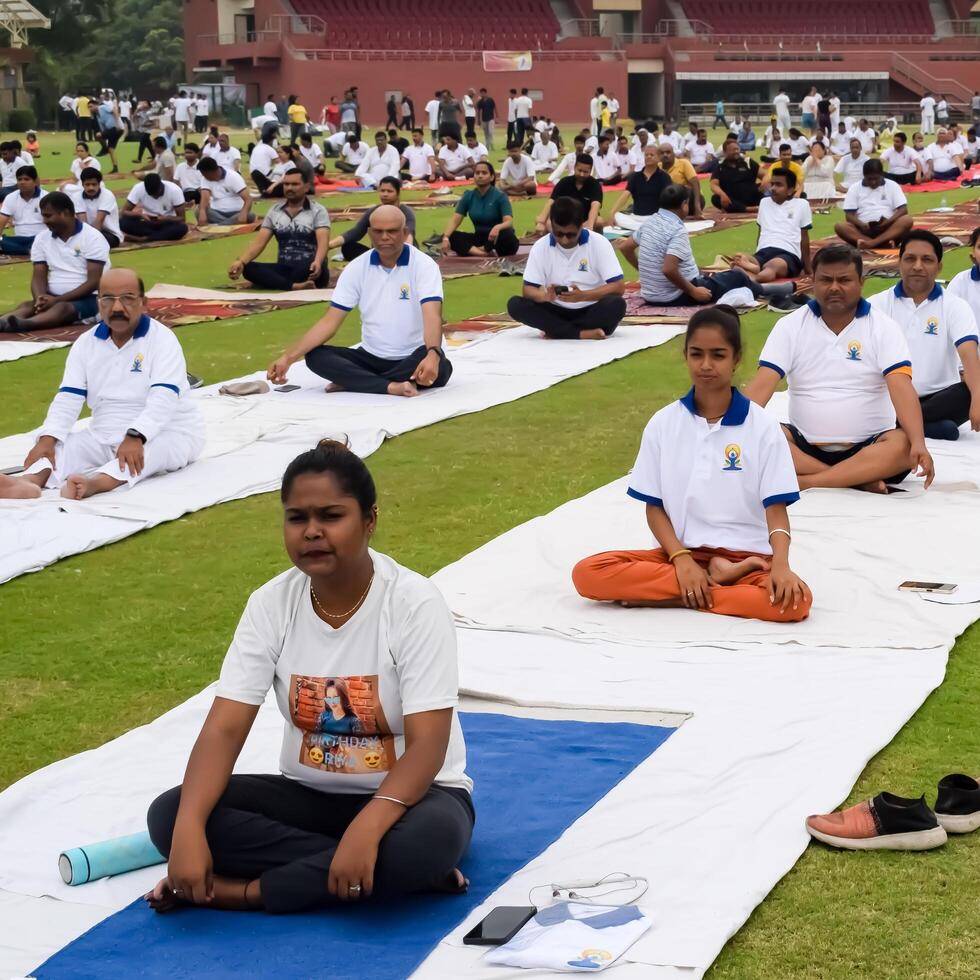 New Delhi, India, June 21, 2023 - Group Yoga exercise session for people at Yamuna Sports Complex in Delhi on International Yoga Day, Big group of adults attending yoga class in cricket stadium photo