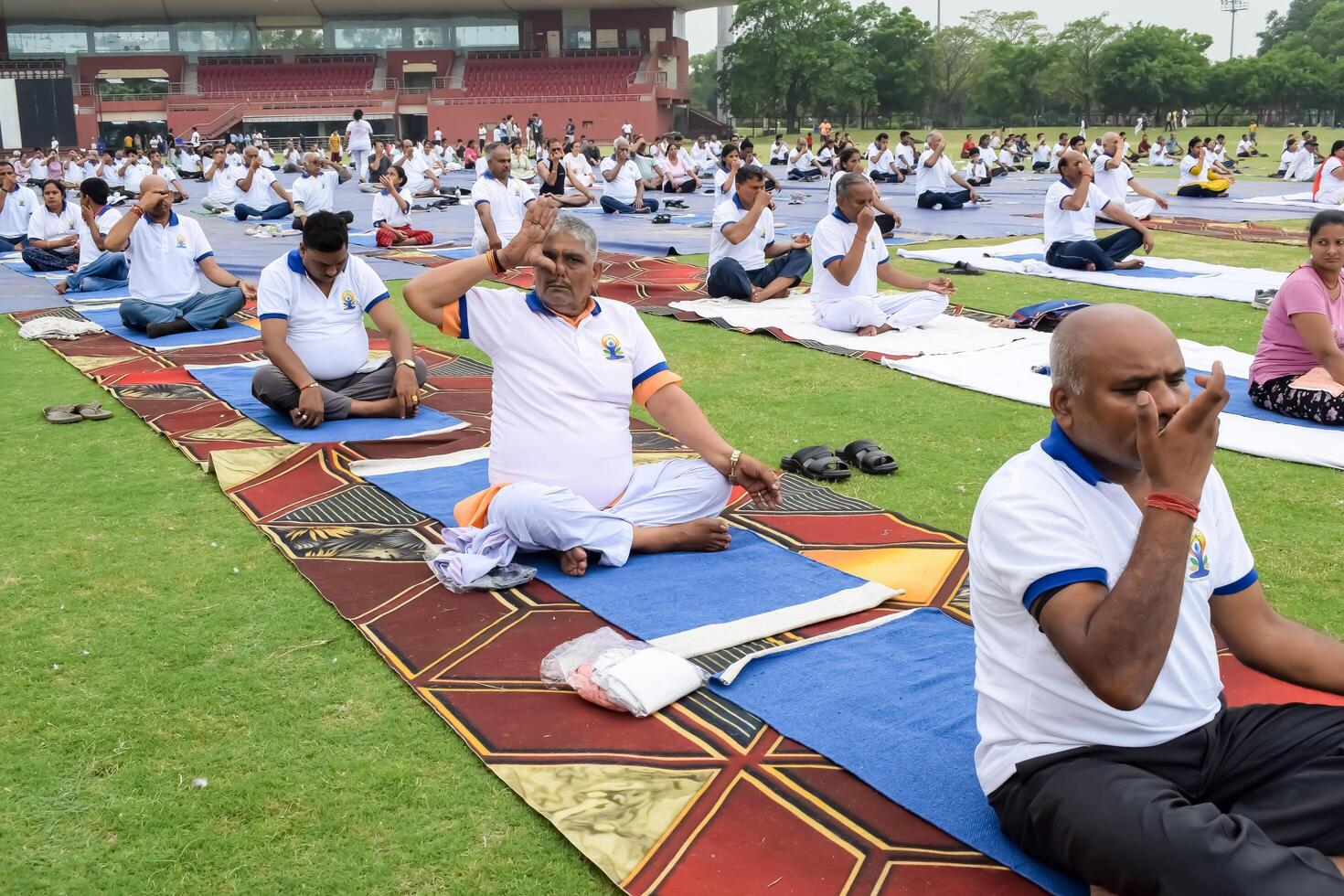 New Delhi, India, June 21, 2023 - Group Yoga exercise session for people at Yamuna Sports Complex in Delhi on International Yoga Day, Big group of adults attending yoga class in cricket stadium photo