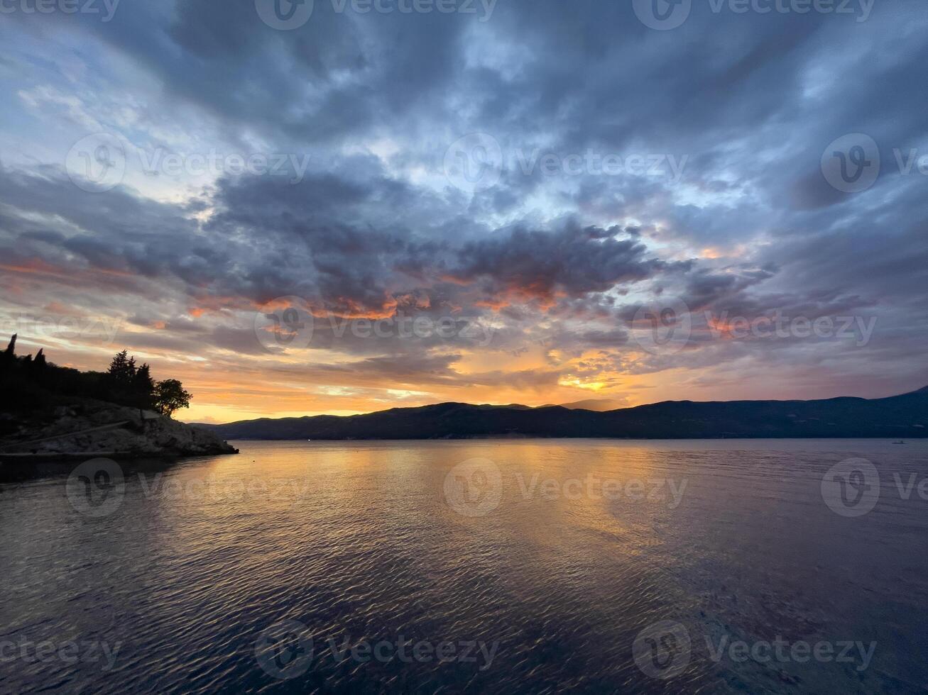 sunset over the sea with clouds and mountains in the background photo