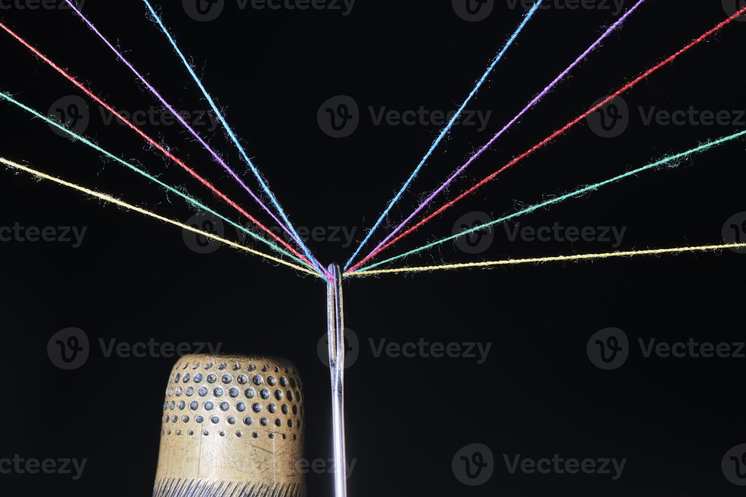 Thimble, eye sewing needle and multicolored threads passed through it black background. photo