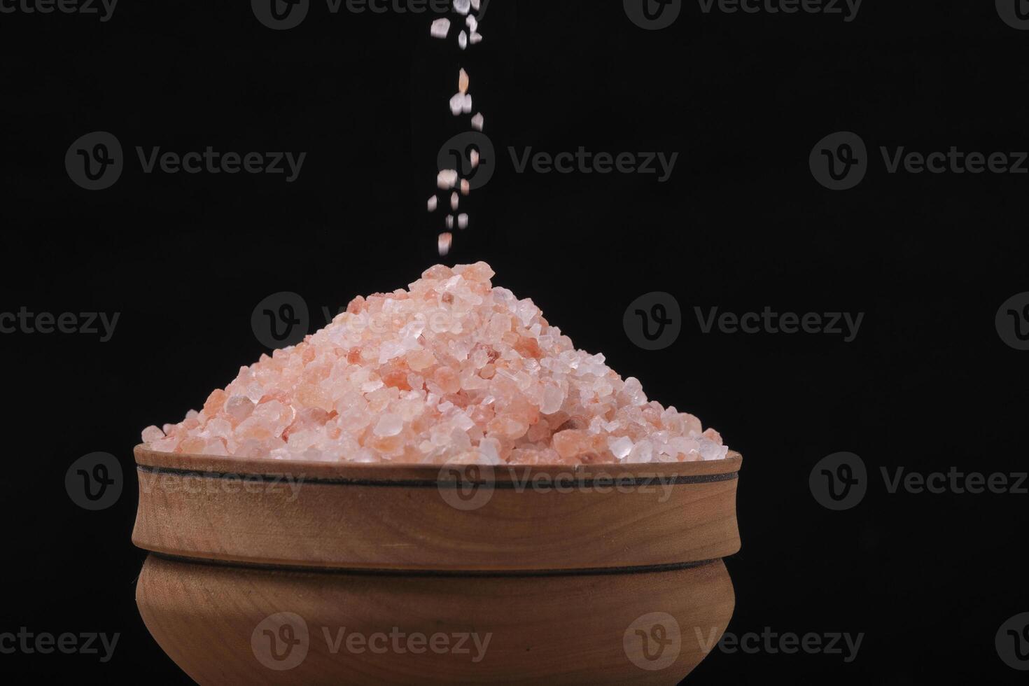 Pouring pink salt into wooden cup black background. photo