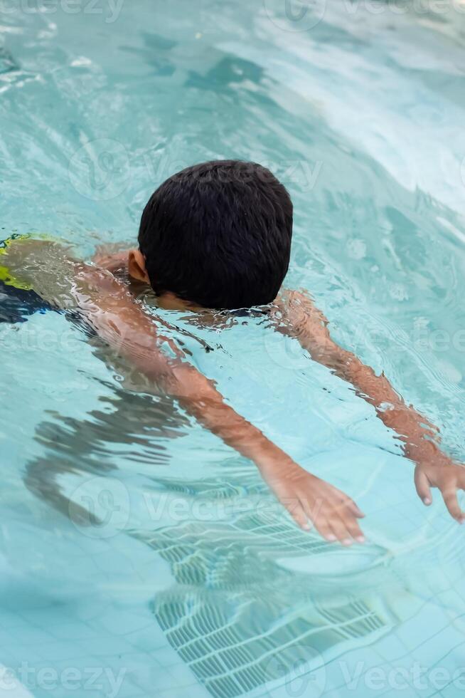 Happy Indian boy swimming in a pool, Kid wearing swimming costume along with air tube during hot summer vacations, Children boy in big swimming pool. photo