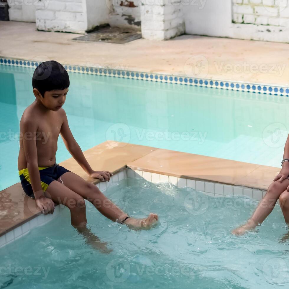 Happy Indian boy swimming in a pool, Kid wearing swimming costume along with air tube during hot summer vacations, Children boy in big swimming pool. photo