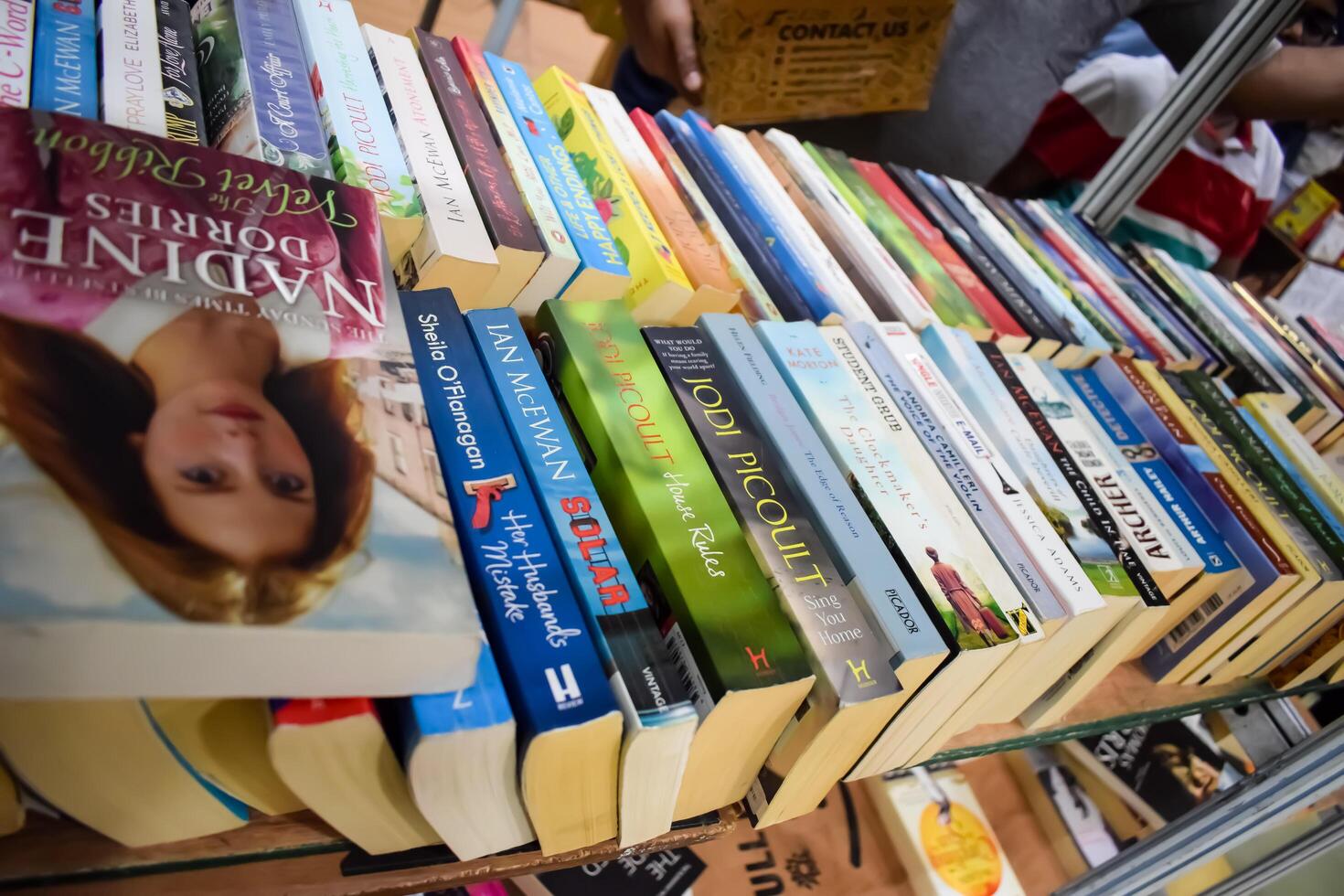 Delhi, India, February 17 2024 - Various age group people reading variety of Books on shelf inside a book-stall at Delhi International Book Fair, Books in Annual Book Fair at Bharat Mandapam complex photo