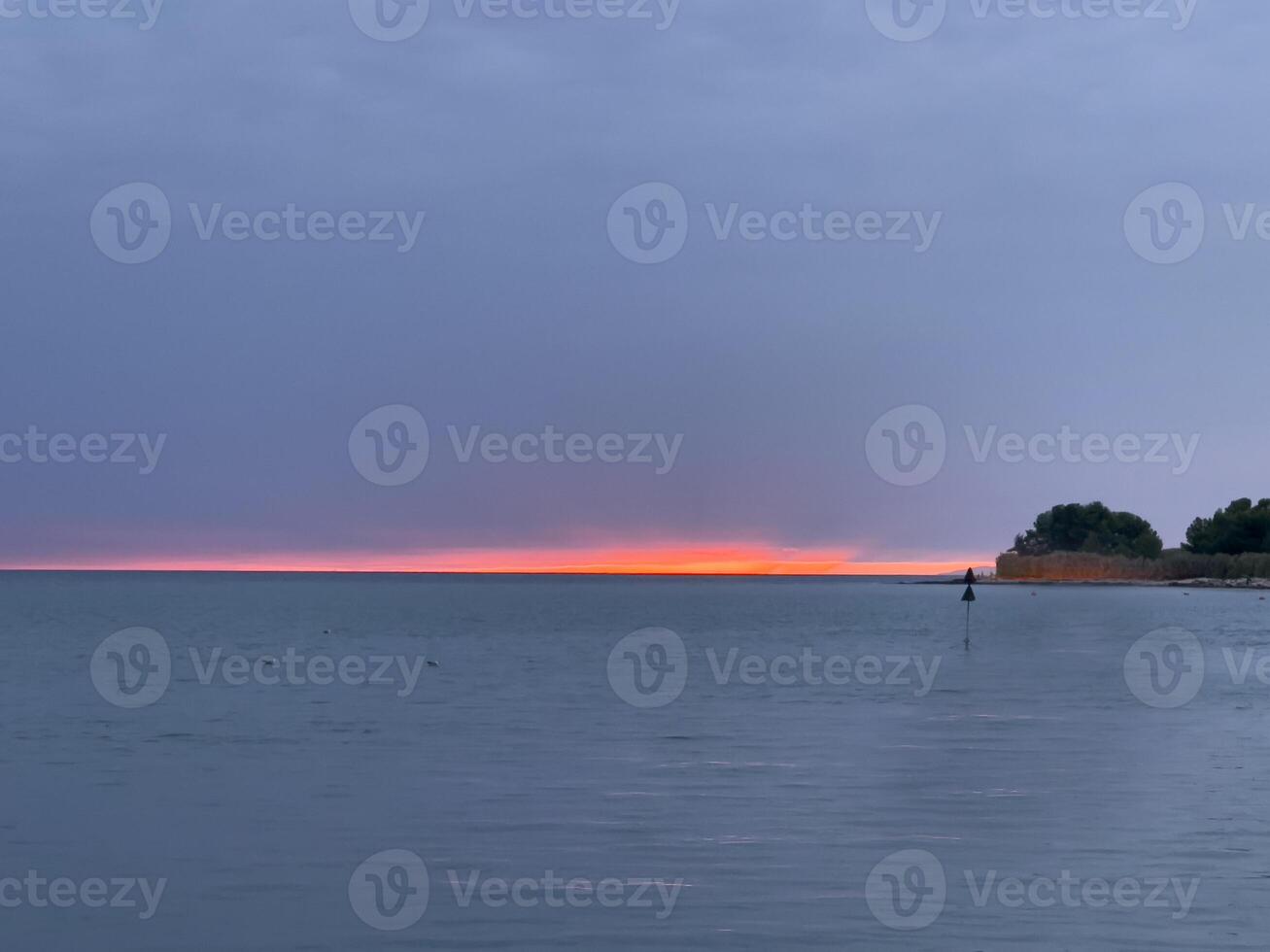 a sunset over the water with a lighthouse in the distance photo