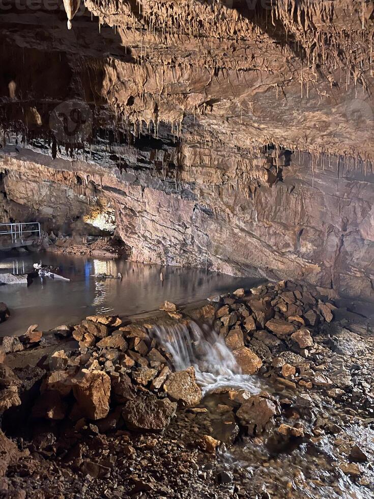 a cave with water flowing through it and people standing around photo